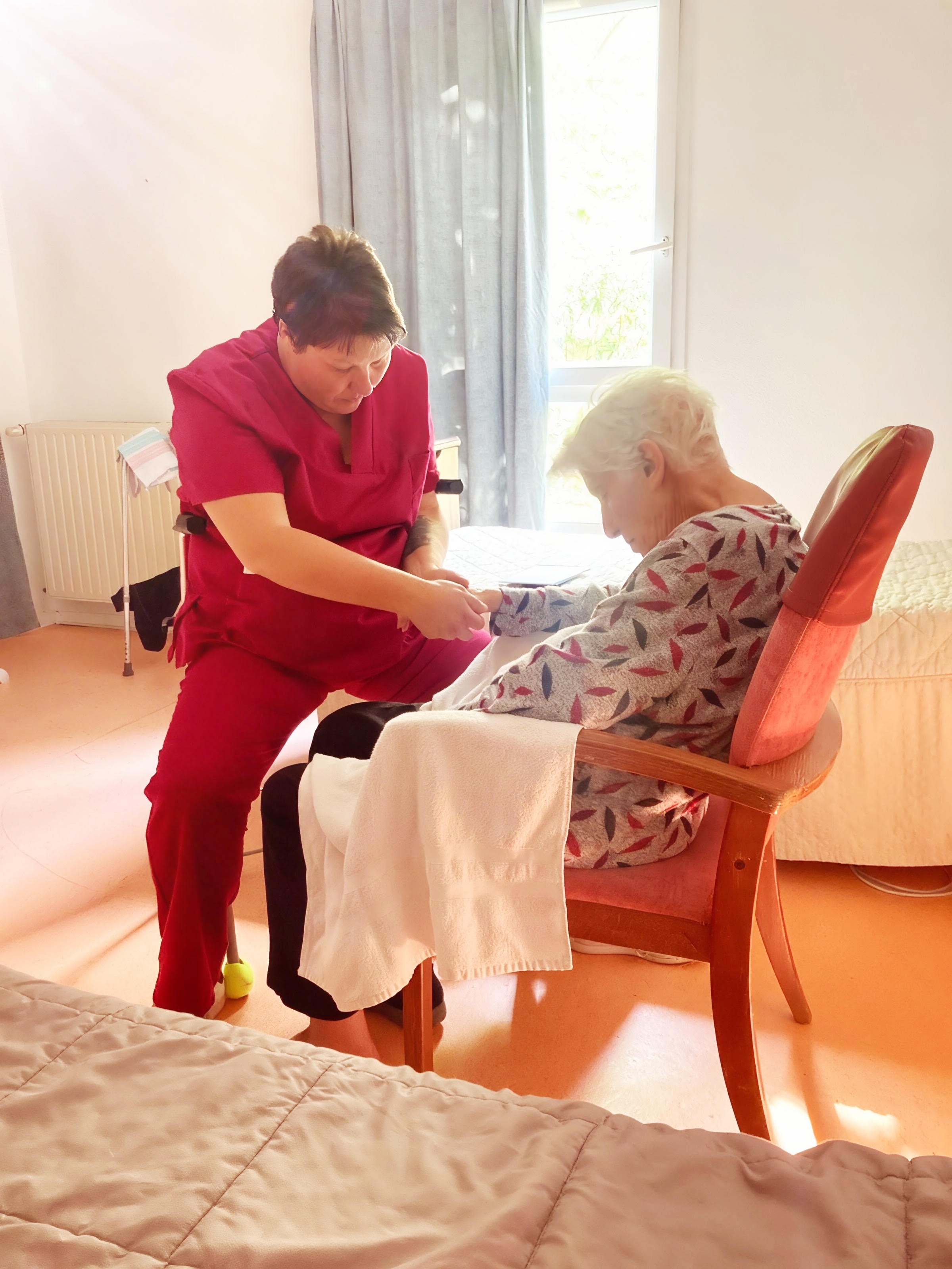Adeline accompagne avec douceur une personne âgée assise.